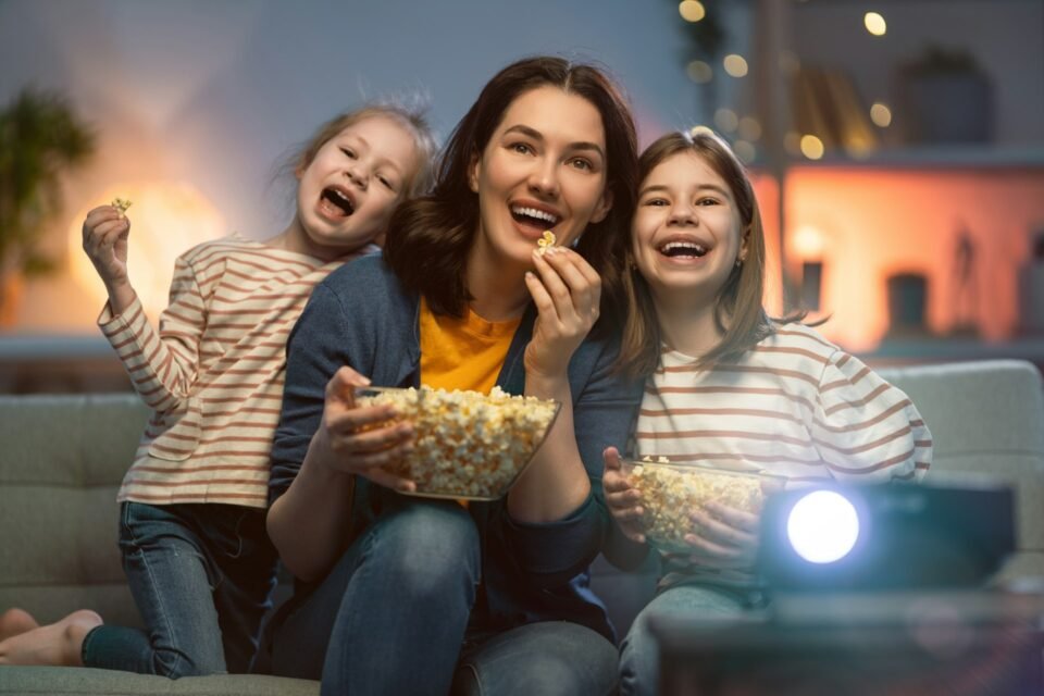 Mother and two children eating popcorn while watching a film at home